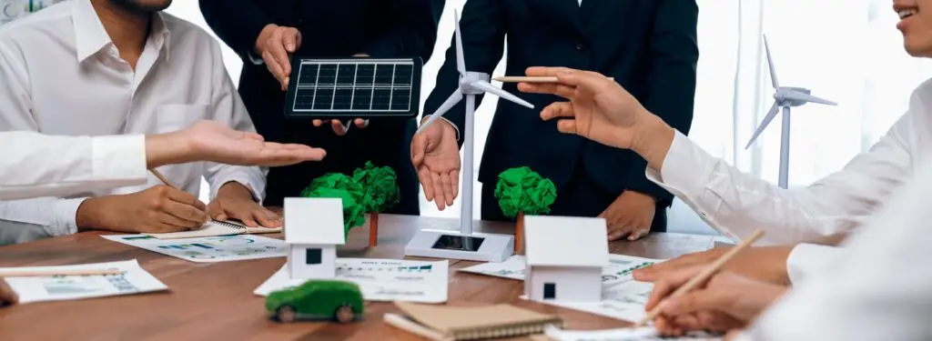 Team of professionals in a meeting with solar panel, wind turbine models, and green economy sketches on the table, promoting green energy business.