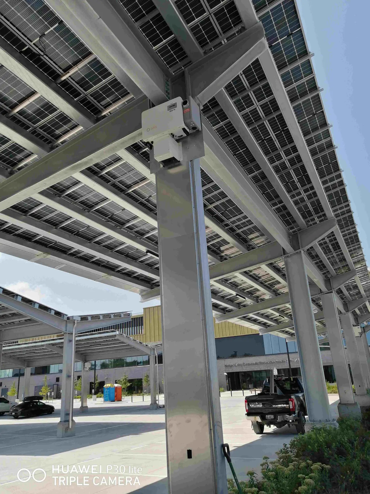 Solar panel carport structure with reinforced steel columns and mounted electrical hardware under a clear sky.