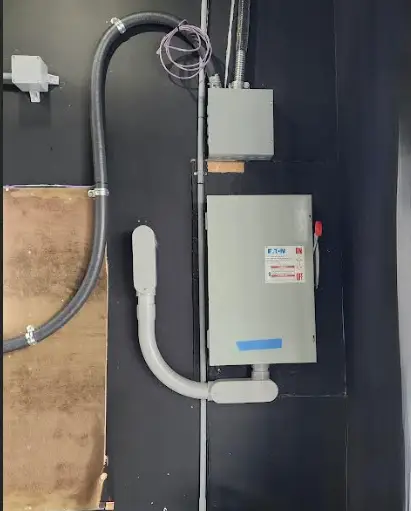 Electrical junction box and conduit on a dark wall, with a curved white conduit and exposed wiring.