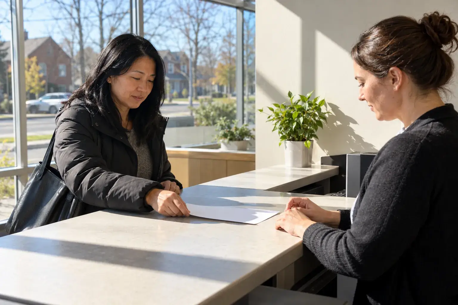 Two women sit across from each other at a light counter, reviewing a document together.